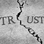 Black and white image of the word "TRUST" split by a large crack in concrete.