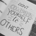 Open notebook with graph paper, handwritten message "Don't compare yourself to others," and date tabs.