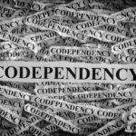 Black and white image of torn paper strips, many reading "Codependency," surrounding a central strip with the same word in bold, black letters.