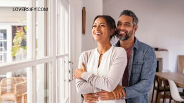 A smiling couple embraces while looking out a window.