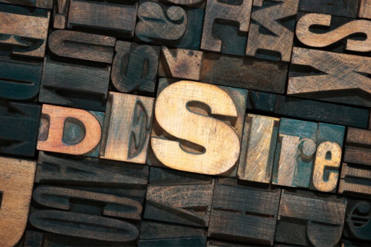 Wooden letterpress blocks spelling "Desire" amidst other jumbled blocks.