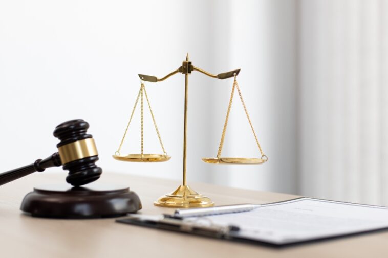 Gavel, scales of justice, pen, and document on a light wooden surface.
