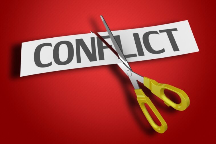Against a red background, scissors with yellow handles cut a white strip of paper with the word "CONFLICT" printed in gray.