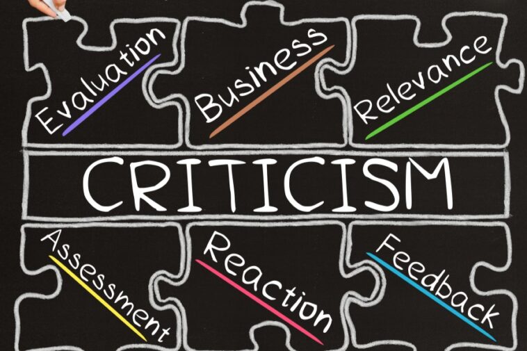 Chalkboard drawing shows the word "Criticism" surrounded by puzzle pieces labeled "Evaluation," "Business," "Relevance," "Assessment," "Reaction," and "Feedback," each with a colored line through it. A hand holds a chalk piece at the top left.