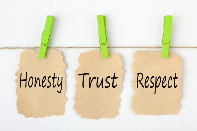 Three tan paper notes with torn edges hang from a twine string, each secured with a bright green clothespin. The words "Honesty," "Trust," and "Respect" are written in black on the notes.
