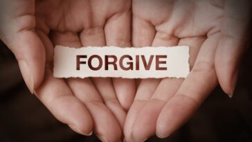 Open hands holding a small, torn piece of paper with the word "FORGIVE" printed on it.