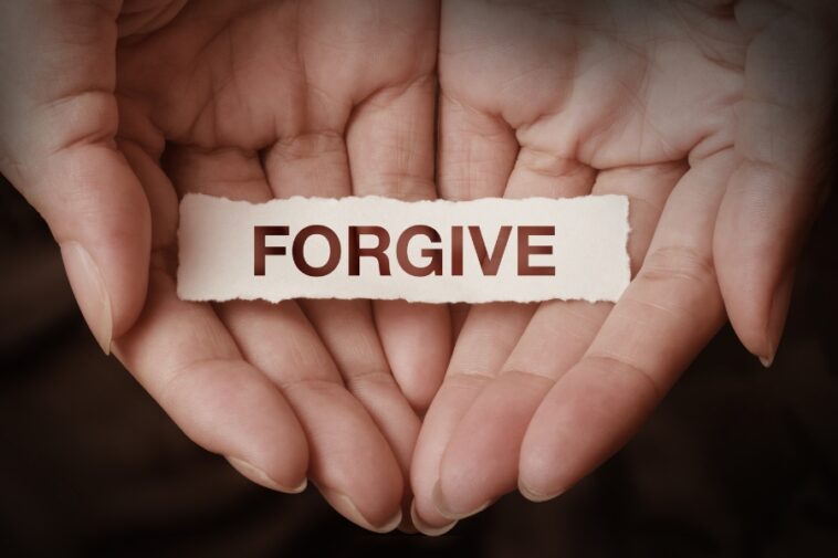 Open hands holding a small, torn piece of paper with the word "FORGIVE" printed on it.