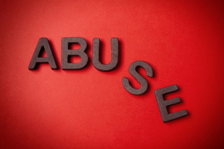 Dark gray block letters spelling "ABUSE" are arranged on a textured red surface.