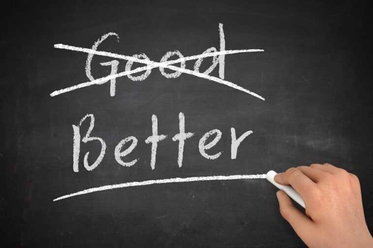 Chalkboard with the word "Good" crossed out and "Better" underlined by a hand holding chalk.