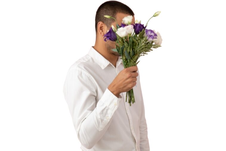 Person in a white shirt holding a bouquet of purple and white flowers in front of their face.