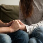 Close-up of a man and woman seated on a couch, holding hands.
