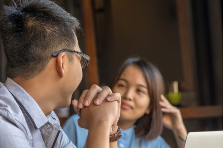 A man with glasses holds another person's hands, while the other person looks at him.