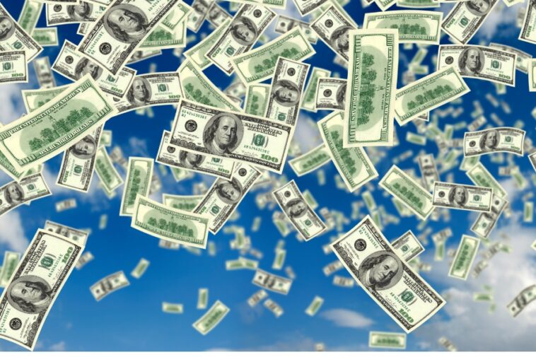 Hundred dollar bills are falling against a blue sky.