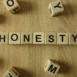 Wooden blocks spell out "HONESTY" on a wood grain surface, surrounded by scattered letter blocks.