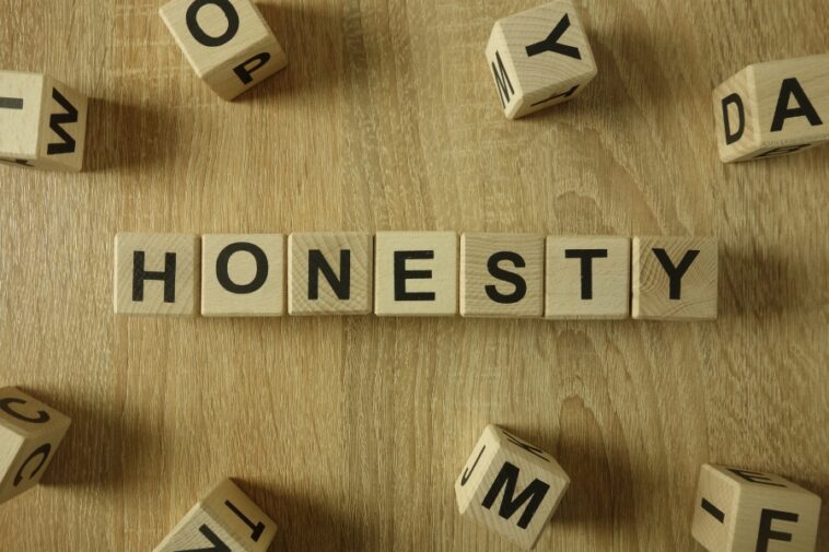 Wooden blocks spell out "HONESTY" on a wood grain surface, surrounded by scattered letter blocks.