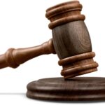 A wooden gavel rests slightly tilted on its matching round base, set against a plain white backdrop.