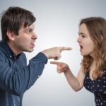 A man and a woman face each other, pointing and yelling.