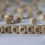 Wooden blocks spell out "RESPECT" in a line, with more blurred blocks scattered in the background.