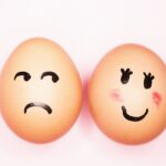 Two eggs with drawn-on faces, one sad and one happy, against a light pink background.