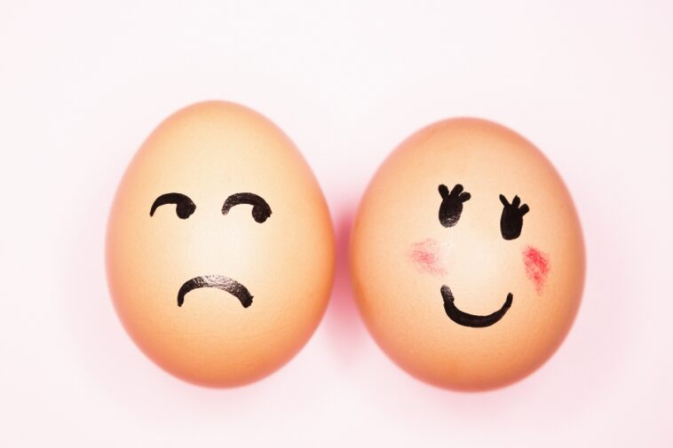Two eggs with drawn-on faces, one sad and one happy, against a light pink background.
