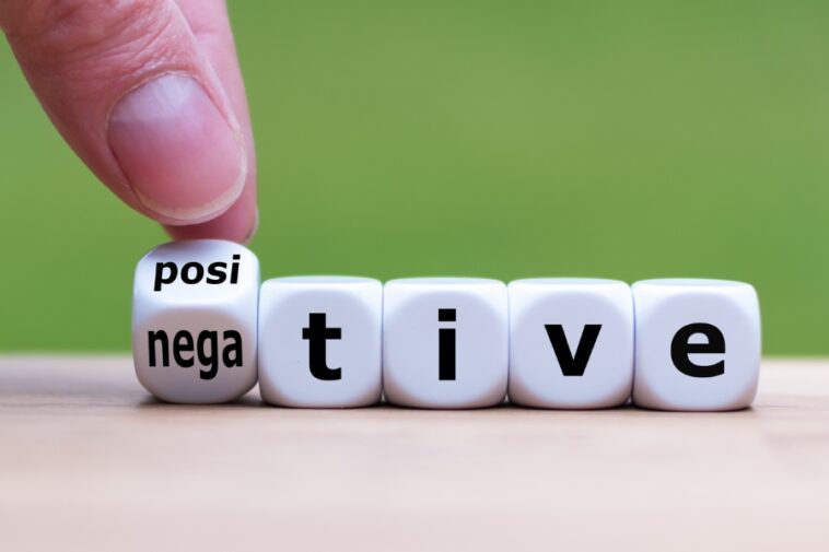 A finger is turning a dice from "negative" to "positive," spelling out the word "positive" with other dice.