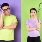 A man and a woman stand side-by-side against a split purple and green background, each with a thought bubble above their heads depicting different romantic scenarios.