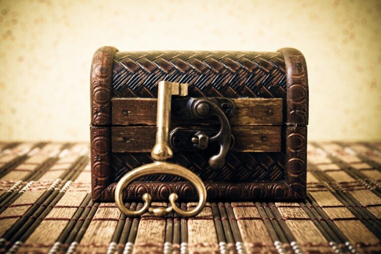 A decorative wooden chest sits on a bamboo mat, with a golden key resting against the chest's latch.