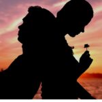 Silhouetted figures of a person leaning against another, holding a small flower, against a sunset sky.