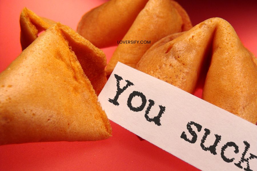 Several fortune cookies on a red surface, one with a paper sticking out that reads "You Suck.