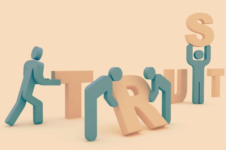 Stylized figures are assembling the word "TRUST" in a light pastel setting.