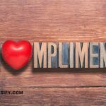 Wooden background with the word "COMPLIMENT" spelled out in block letters, with a red heart replacing the "O".