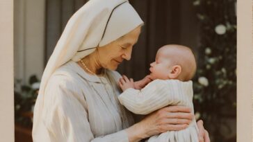 An older woman in a white head covering and dress holds a baby, both facing each other.