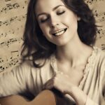 A smiling woman with closed eyes holds a guitar, with musical notes in the background.