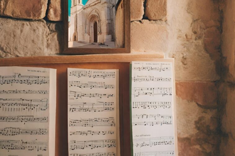 Sheets of music sit below a framed picture of a stone building. The background is a stone wall.