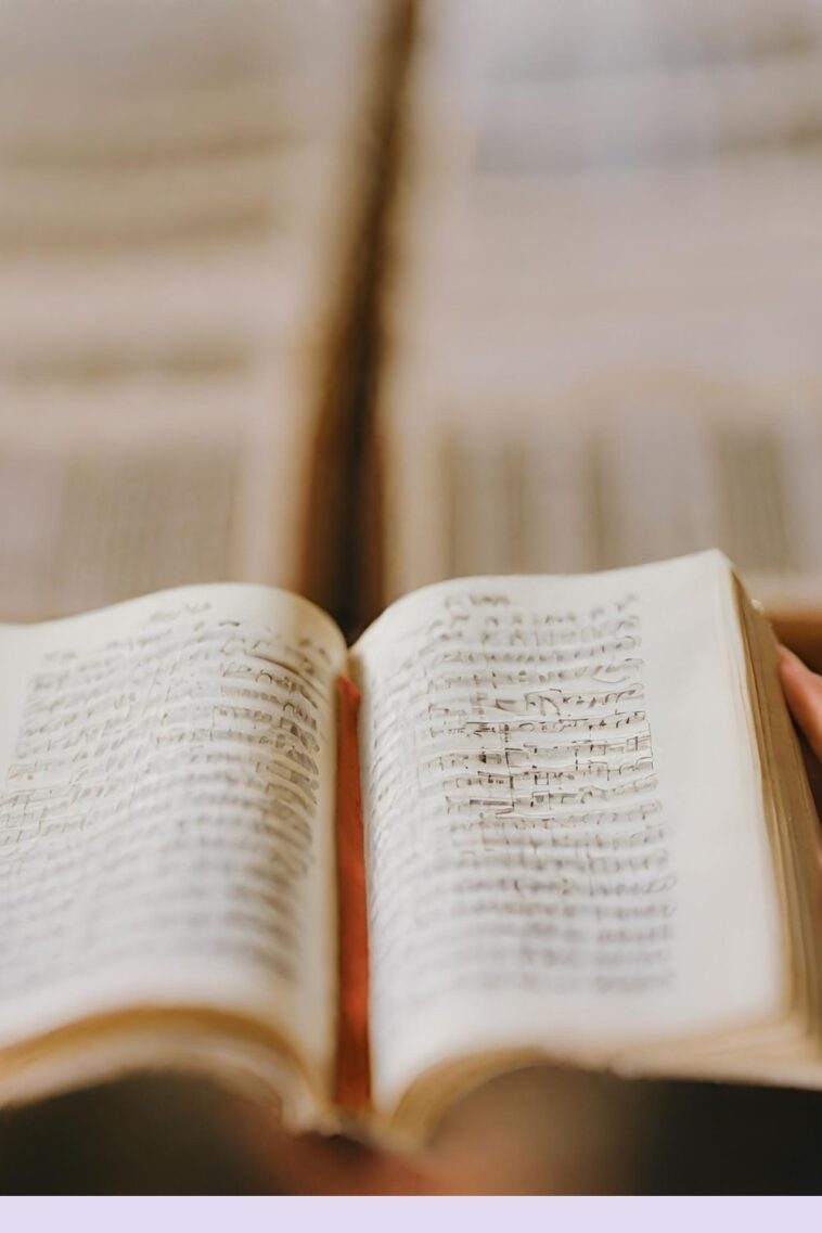 Open book with handwritten musical notation, red ribbon bookmark, and another book blurred in the background.