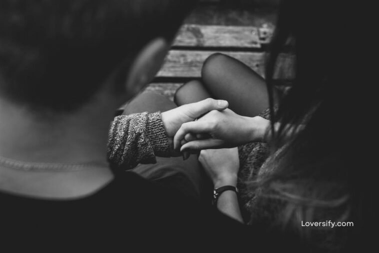 Black and white, close-up view from above shows a couple sitting with hands intertwined.