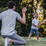 Father and son play baseball in a park; father pitches while son holds a bat.