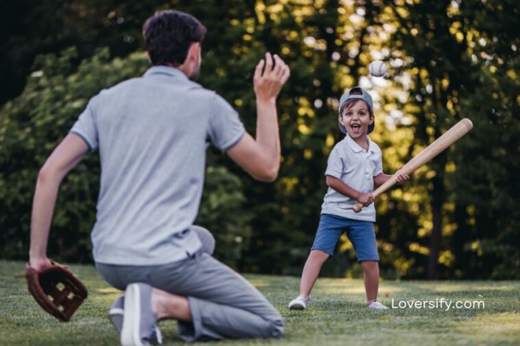 Father and son play baseball in a park; father pitches while son holds a bat.