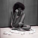 Person with curly hair sits on the floor surrounded by tissues.
