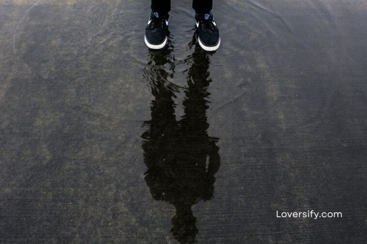 Person wearing sneakers standing in shallow water, their reflection visible.