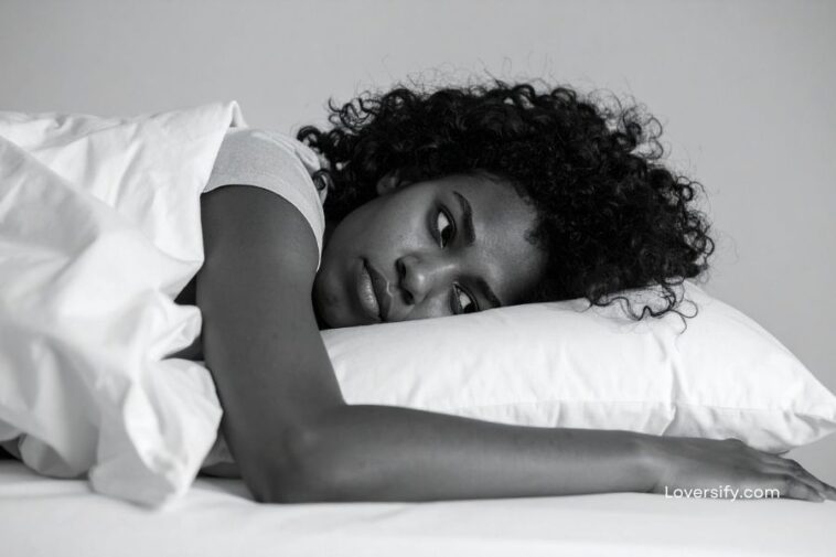 Black and white shot of a woman with curly hair lying in bed.