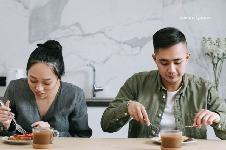 A man and woman sit at a table eating breakfast in a kitchen.