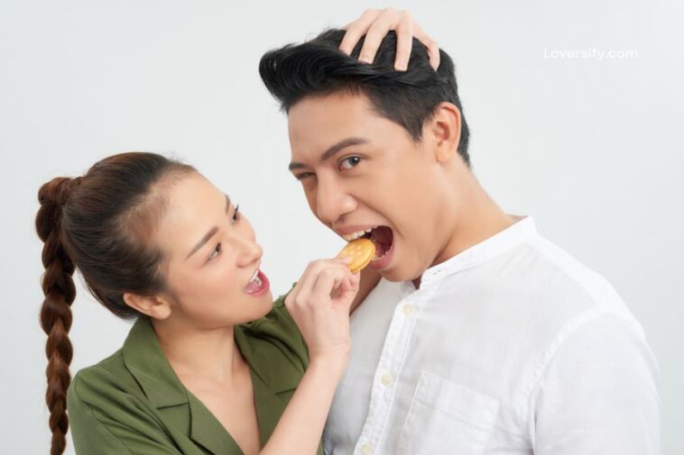 A woman feeds a man a biscuit while he plays with his hair.