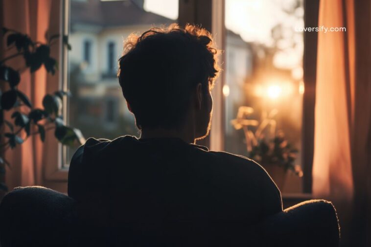 A person sits in silhouette facing a window with the bright sun setting outside.