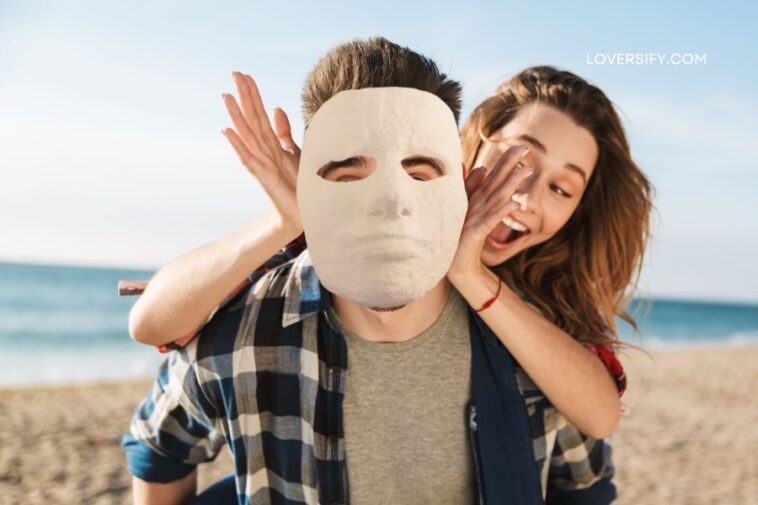 A woman with her hands near the face of a man wearing a white mask on a beach.