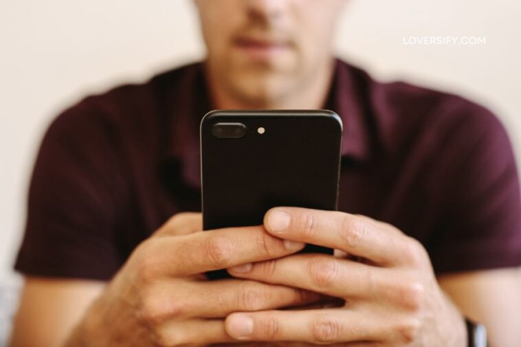 Man wearing a burgundy polo shirt holds a black smartphone.
