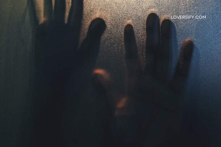 Silhouetted hands press against a frosted glass surface, illuminated by warm light from behind.