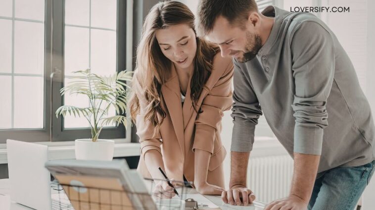 A man and a woman lean over a desk, looking at papers.