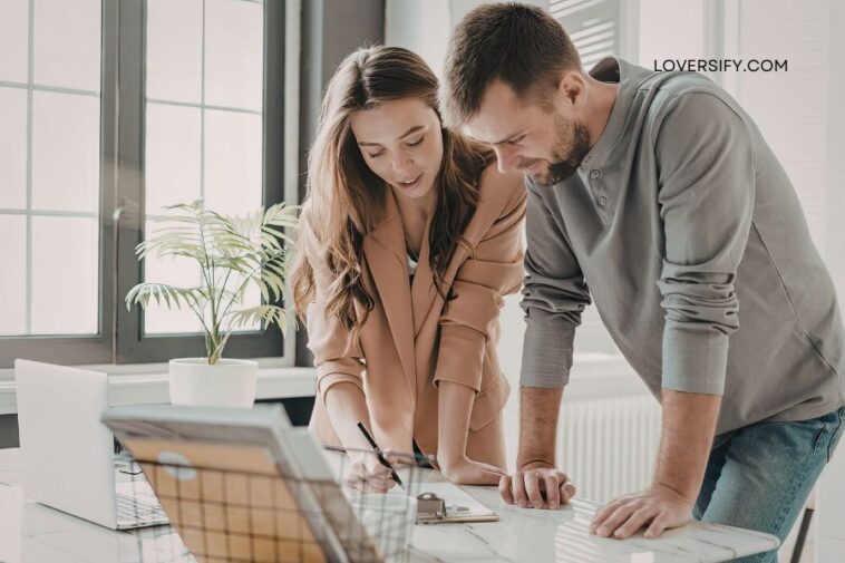 A man and a woman lean over a desk, looking at papers.