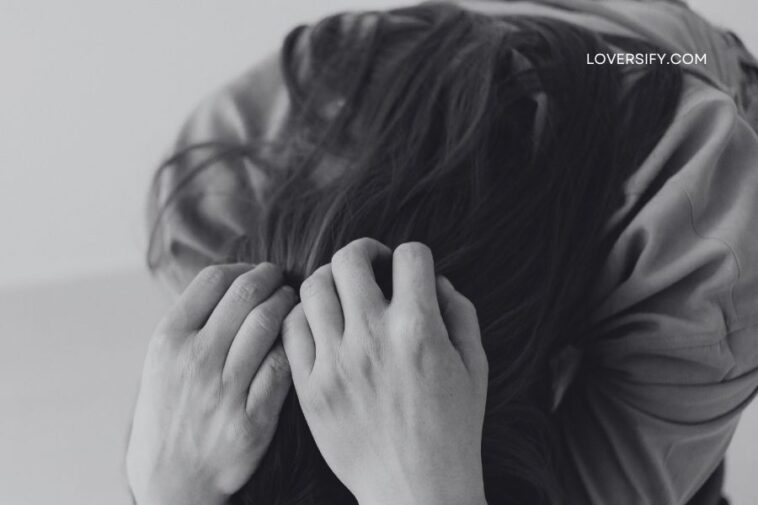Close-up of a person's hands gripping their dark hair, head bowed.